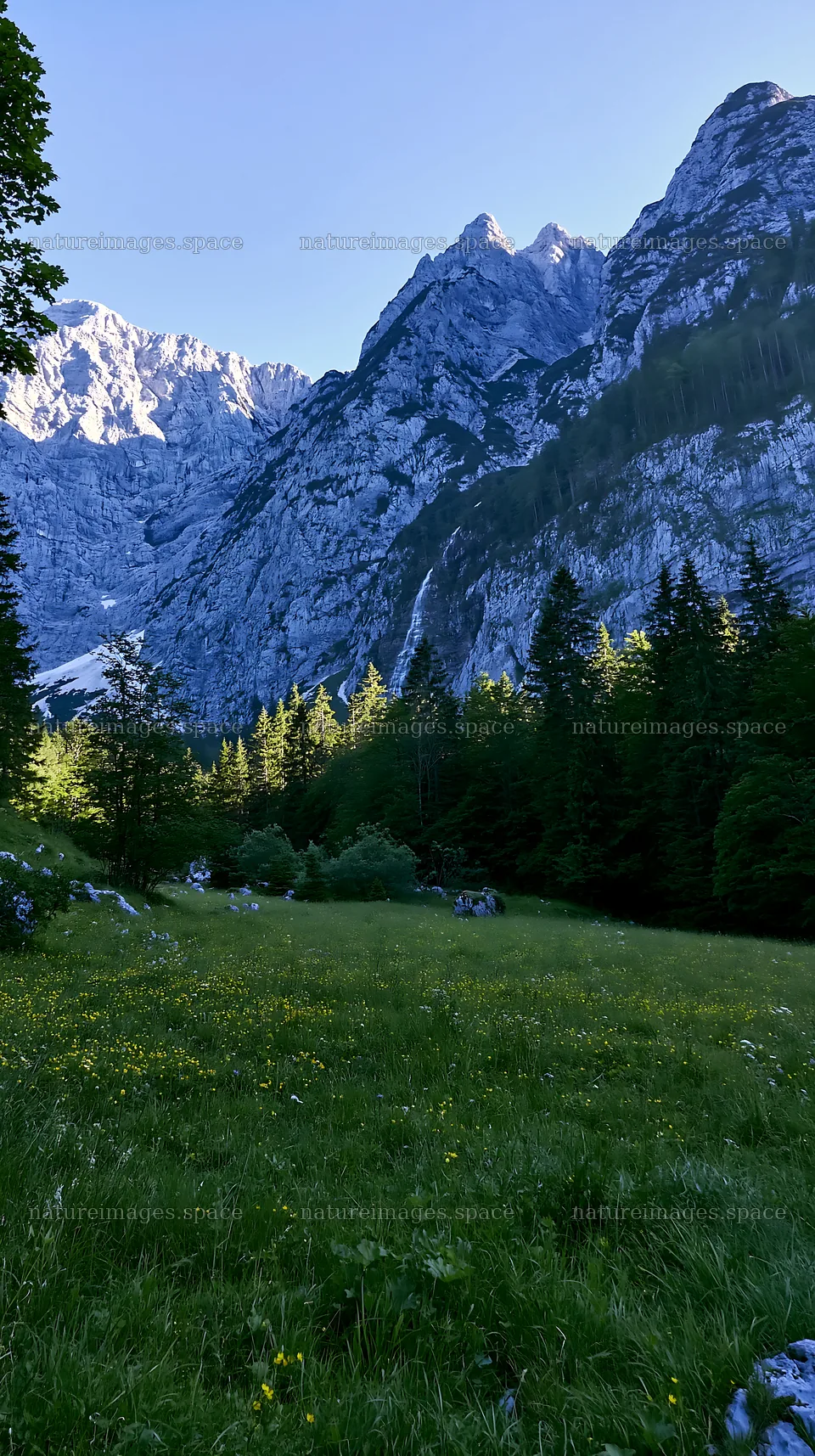 Meadow beneath crags with mountains in the background – nature images 5938x10608