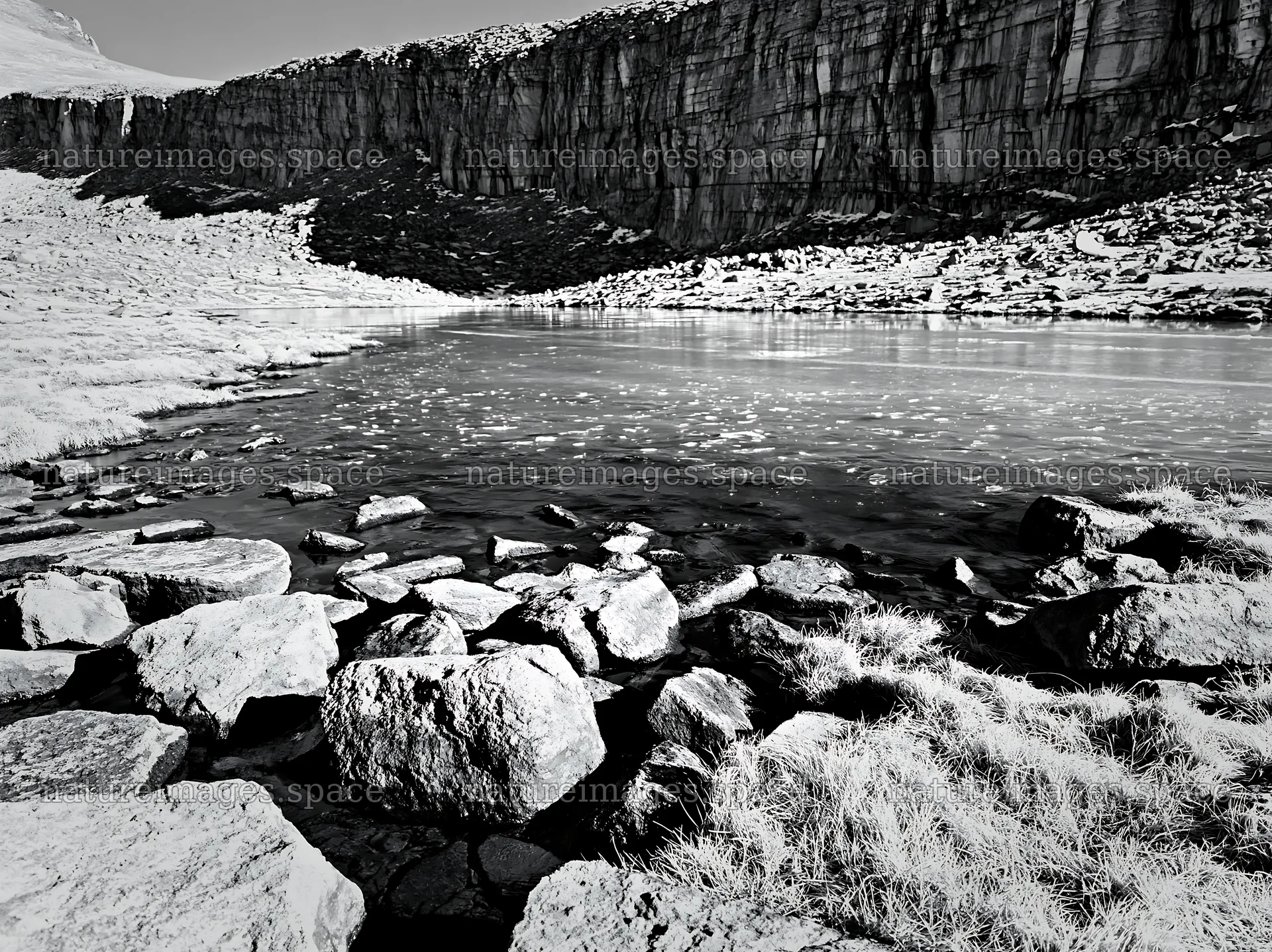 Frozen tarn in a meadow surrounded by rocky cliffs – nature images 9174x6866