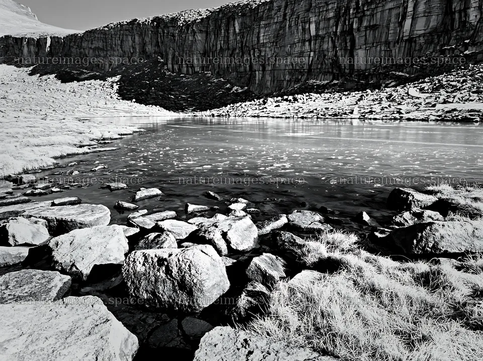 Frozen tarn in a meadow surrounded by rocky cliffs – nature images 9174x6866